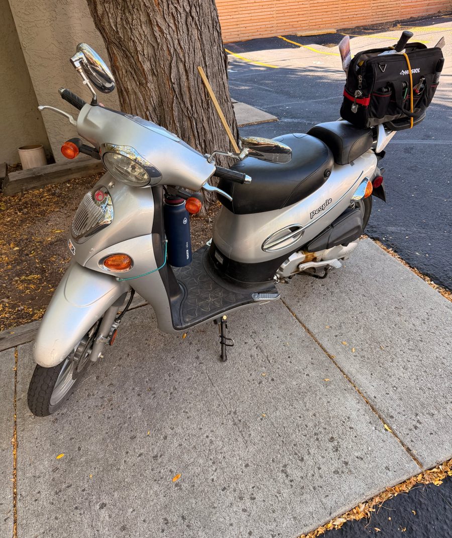 Paul's silver scooter under a Boulder cottonwood, tool bag strapped to the back